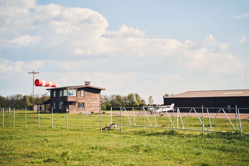 Beautiful view of airfield with small airplane, grassy lawn, buildings and cloudy sky on background