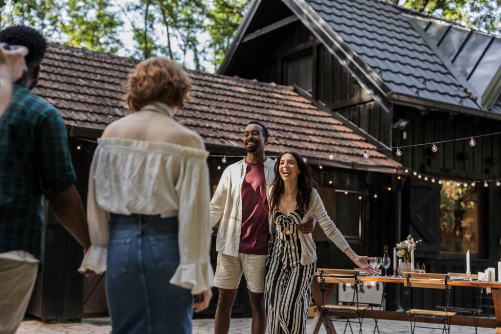 Photographer taking pictures of multiracial friends arriving at a party in a countryside house with string lights and a decorated table
